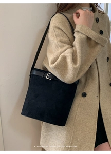 Détail du sac seau noir mat avec boucle en métal argenté sur une veste en tweed