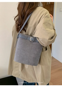 Détail d'un sac seau gris en daim avec boucle et bandoulière sur un mannequin
