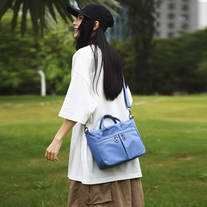 Close-up of a light blue nylon shoulder bag with dual zipper pockets in a park setting