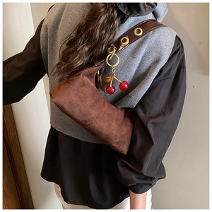 Detail of dark brown suede tote with wide eyelet strap and red cherry charm accessory