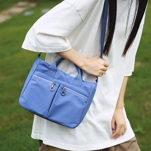 Detail of blue nylon shoulder bag with dual front zippers on a natural grass background