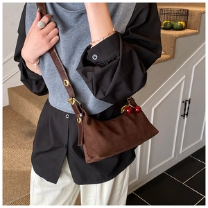 Close-up of brown suede tote bag featuring adjustable leather strap and cherry charm detail