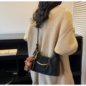 Close-up of black leather crescent bag featuring a gold moon clasp and brown bear charm