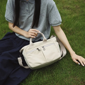 Nylon tote bag detail showing dual front zipper pockets on an outdoor grass lawn