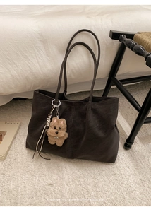 Detail of dark brown matte leather tote bag with woven fringe and plush dog charm
