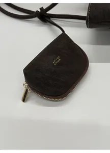 Detalle de mini bolso de cuero marrón oscuro con textura granulada y logo dorado