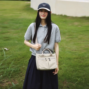 Detail of beige nylon tote bag with dual front zippers shown in outdoor setting
