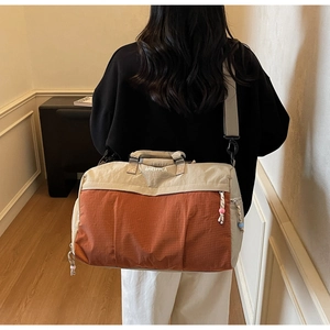 Détail du sac de voyage beige et orange avec logo et curseur de fermeture à perles