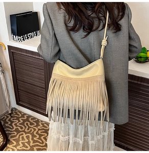 Dettaglio della borsa a secchiello beige con frange indossata da modella in blazer grigio
