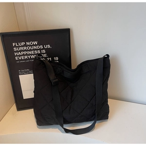 Detailed view of large quilted black nylon tote bag with adjustable woven shoulder strap
