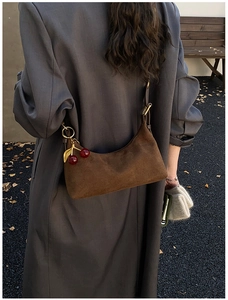 Detail of brown suede hobo bag featuring a red cherry metal charm pendant in outdoor light