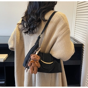 Detail of black croissant bag featuring a golden metal buckle and a cute brown plush bear