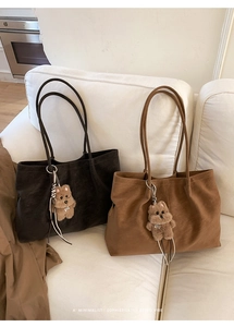 Close-up of retro matte leather tote bags with cute plush bear charms on a sofa