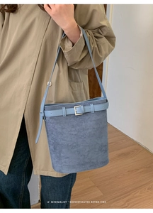 Détail du sac seau en daim bleu avec boucle en cuir porté sur un trench-coat beige