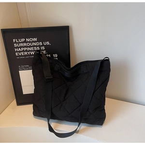 Detail of black quilted tote bag with large diamond stitching and adjustable strap