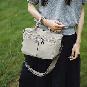 Outdoor shot of a beige nylon tote bag with dual front zippers and adjustable wide strap