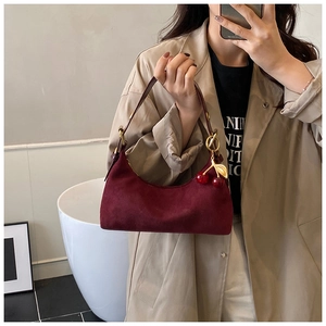 Detail of burgundy suede tote bag featuring a decorative cherry charm and gold hardware