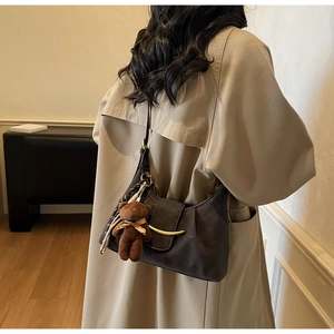 Detail view of coffee crescent shoulder bag with gold buckle and cute bear pendant charm