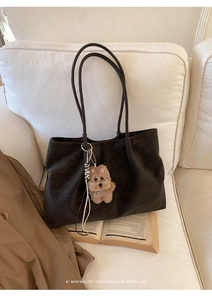 Detail of retro large brown leather tote bag with plush puppy charm on a soft sofa