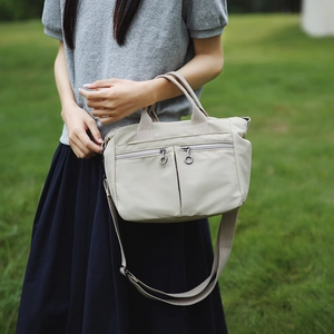 Detail of light beige nylon tote bag featuring front dual zipper pockets and round pullers