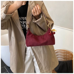 Detail of burgundy suede crescent bag with elegant metal cherry pendant and gold hardware