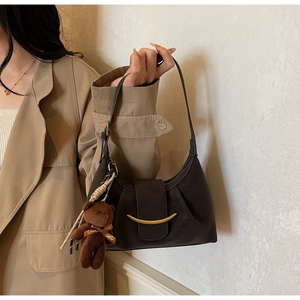 Detail of dark coffee croissant bag with golden buckle and cute plush bear charm