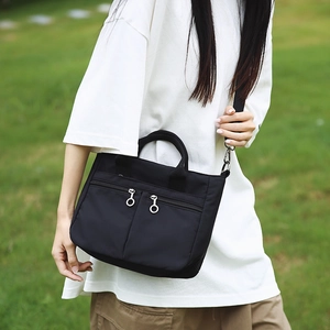 Outdoor shot of a black nylon crossbody bag featuring double front zip pockets and metal rings