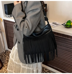 Dettaglio ravvicinato di una borsa a secchiello in pelle nera con frange e tracolla annodata