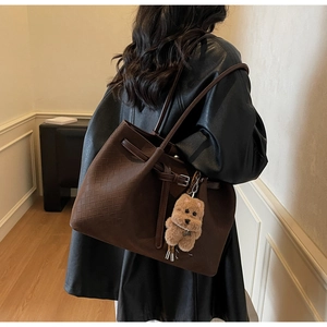 Detail of dark brown woven tote bag featuring belt buckle and plush bear charm