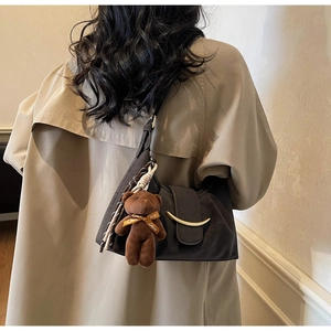 Close-up of a dark brown dumpling bag with gold hardware and a cute plush bear charm