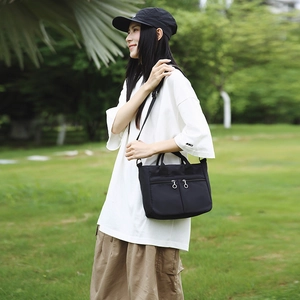 Detailed view of lightweight black nylon shoulder bag with multiple zippered pockets outdoors