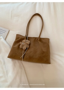 Detail of a brown vintage tote bag with litchi texture and a cute plush bear pendant