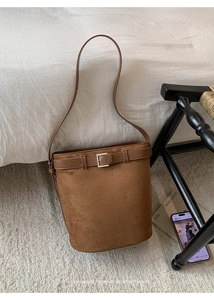 Gros plan du sac seau en daim marron avec boucle métallique dans un décor d'intérieur