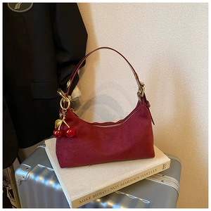 Detail of burgundy suede crescent bag featuring golden hardware and cherry charm