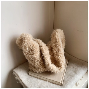 Detail view of beige plush bucket bag on white knit blanket showing soft faux fur texture