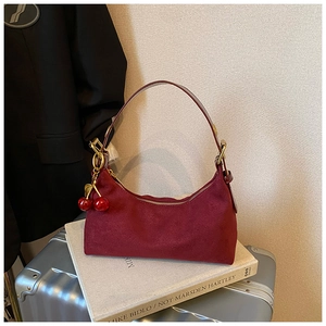 Detail of burgundy suede hobo bag featuring cherry charm and golden metal hardware