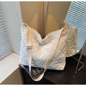 Close-up of white quilted tote bag with diamond stitching and wide fabric shoulder strap