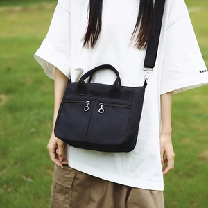 Detail of black nylon crossbody bag with double front zippers and a wide fabric strap