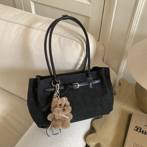 Detail of black matte tote bag with teddy bear charm on cozy beige sofa background