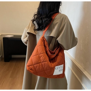 Macro view of bright orange quilted tote bag featuring a stitched brand label and nylon fabric