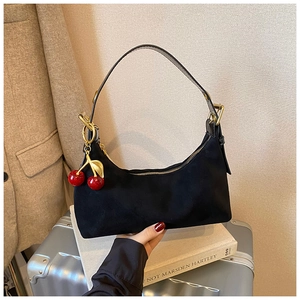 Detail of black suede crescent tote bag with red cherry charm on a stylish background
