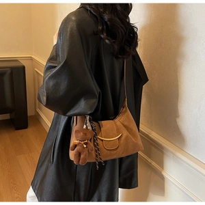 Detail of brown dumpling bag with golden crescent clasp and plush bear charm decoration