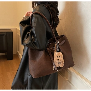 Detail of dark brown tote bag featuring woven texture and a cute plush puppy charm