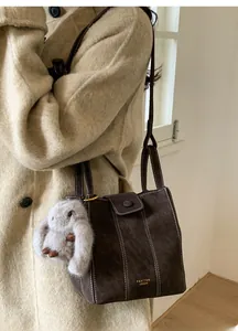 Dark brown suede bucket bag with contrast stitching and a plush rabbit charm accessory