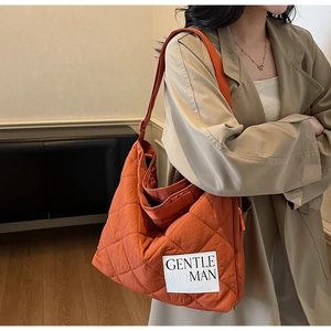 Close-up of orange quilted tote bag featuring a branded label and adjustable wide strap
