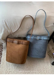 Détail de sacs seaux en daim mat marron et bleu-gris avec boucles métalliques