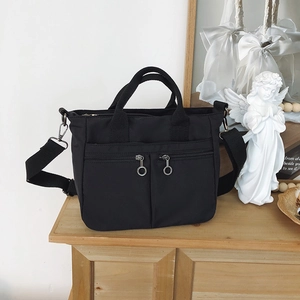 Close-up of black nylon tote bag featuring dual front zipper pockets and round metal pulls