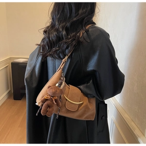 Close-up of brown crescent crossbody bag with gold hardware and a cute plush bear charm