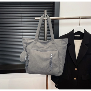 Dettaglio borsa tote in velluto a coste grigio con tasca a zip e ciondolo rotondo