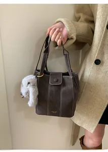 Close-up of retro brown bucket bag with white contrast stitching and plush rabbit charm